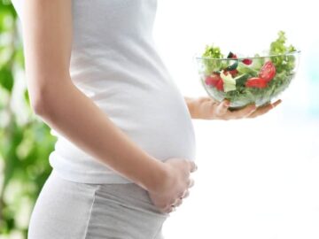 Femme enceinte tenant son ventre d'une main et un bol de salade de l'autre