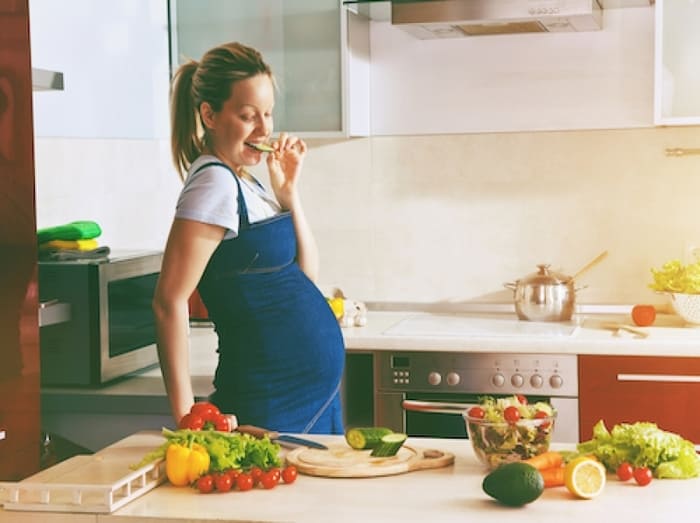 Femme enceinte dégustant un morceau concombre dans sa cuisine