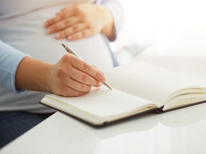 Jeune femme enceinte se tenant le ventre d'une main et écrivant dans son journal d'une autre main
