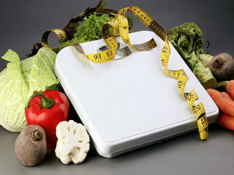 Régime Dukan Pèse personne posé sur des fruits et légumes enlacés par un mètre ruban