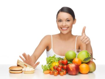 Femme repoussant des sandwiches d'une main et approuvant des fruits et légumes de l'autre main