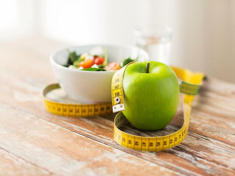 Perdre du poids Assiette remplie et pomme entourées par un mètre ruban