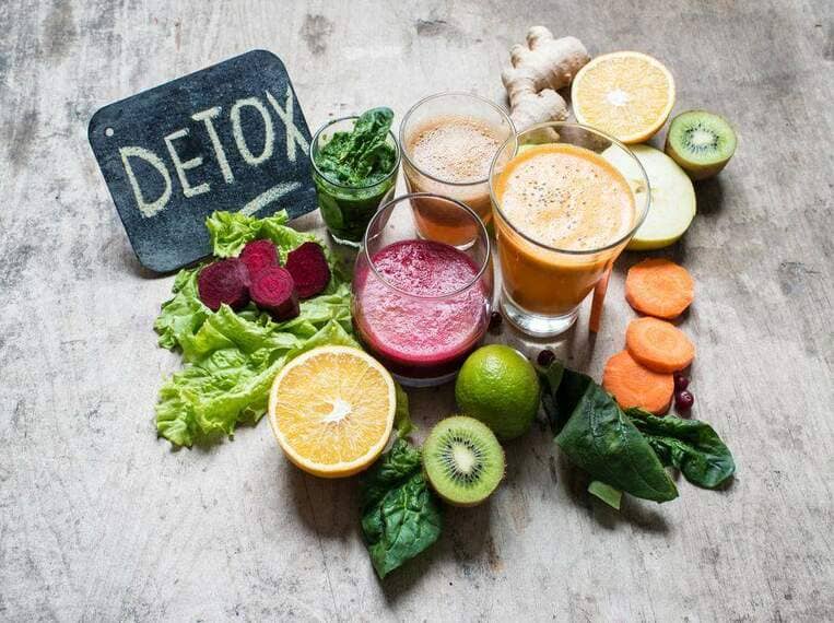 Boisson detox Fruits et légumes disposés aux côtés de verres de jus et d'une ardoise sur laquelle est écrit Detox