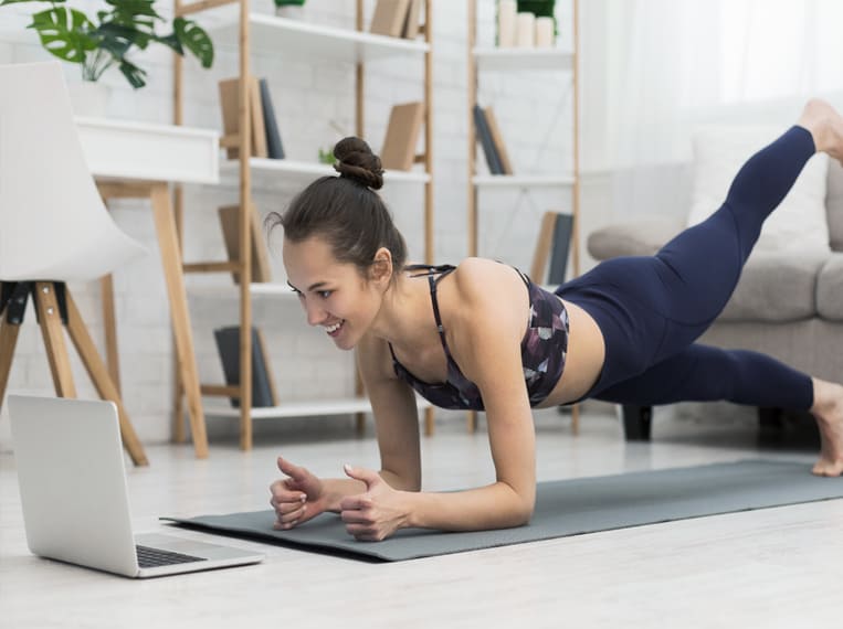 Jeune femme réalisant l'exercice de la planche dans son salon sur son tapis de yoga